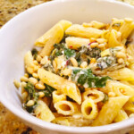 Penne with beet greens, artichokes and pine nuts in a creamy goat cheese sauce in a white bowl