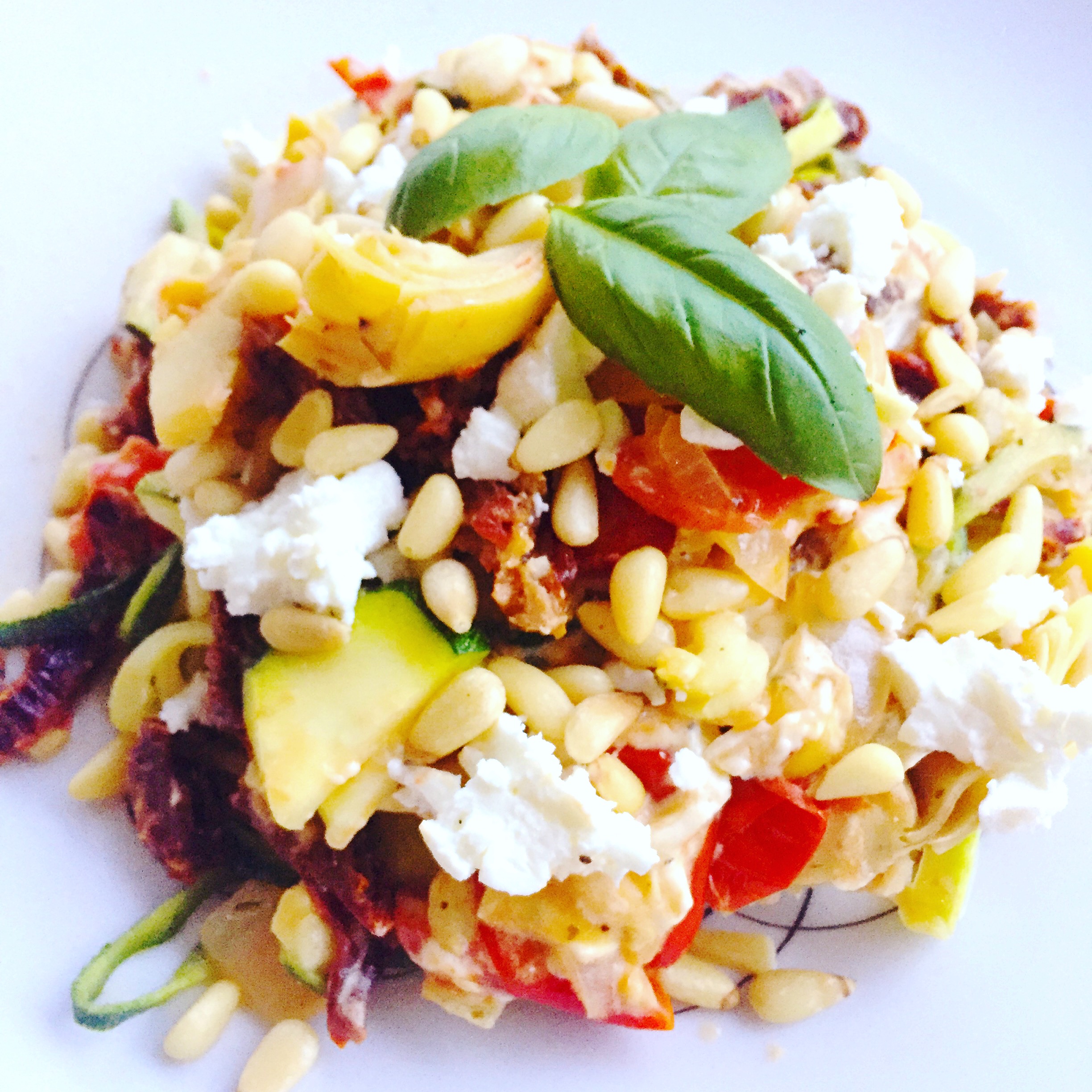 Zucchini noodles with sun-dried tomatoes, goat cheese and pine nuts on a white plate