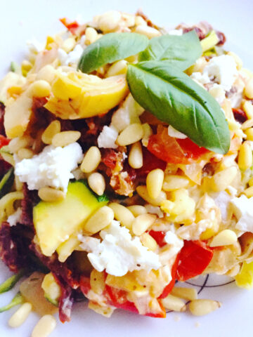 Zucchini noodles with sun-dried tomatoes, goat cheese and pine nuts on a white plate