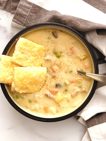 chicken pot pie soup in a bowl with pie crust crackers and a spoon in bowl on a marble counter with a striped napkin.