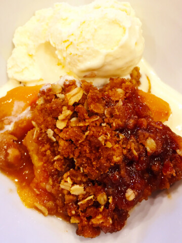 Peach crisp with vanilla ice cream in a white bowl