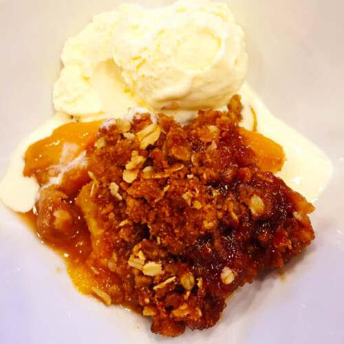 Palisade Peach Crisp in bowl with a scoop of vanilla ice cream