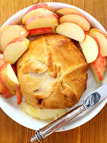 Raspberry baked brie in a white dish with sliced apples on a wood table.