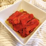Roasted red bell peppers in a white bowl covered with olive oil.