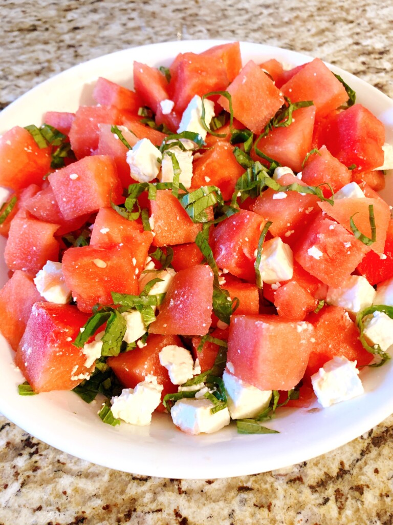 Watermelon cubes, feta cubes and basil ribbons in a white bowl on a granite background