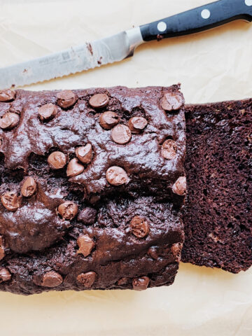 Sliced double chocolate chip banana bread on parchment paper with a bread knife