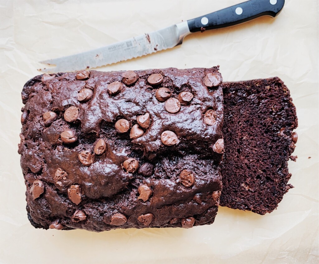 Sliced double chocolate chip banana bread on parchment paper with a knife