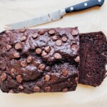Sliced double chocolate chip banana bread on parchment paper with a bread knife