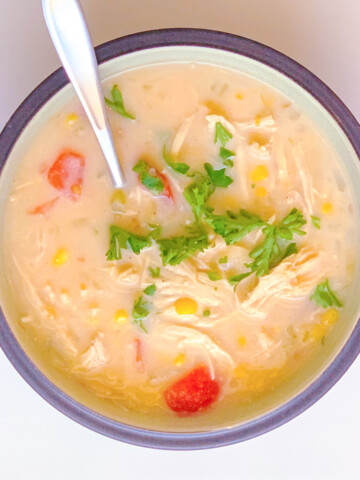 chicken and corn soup in a bowl with a spoon on a white background