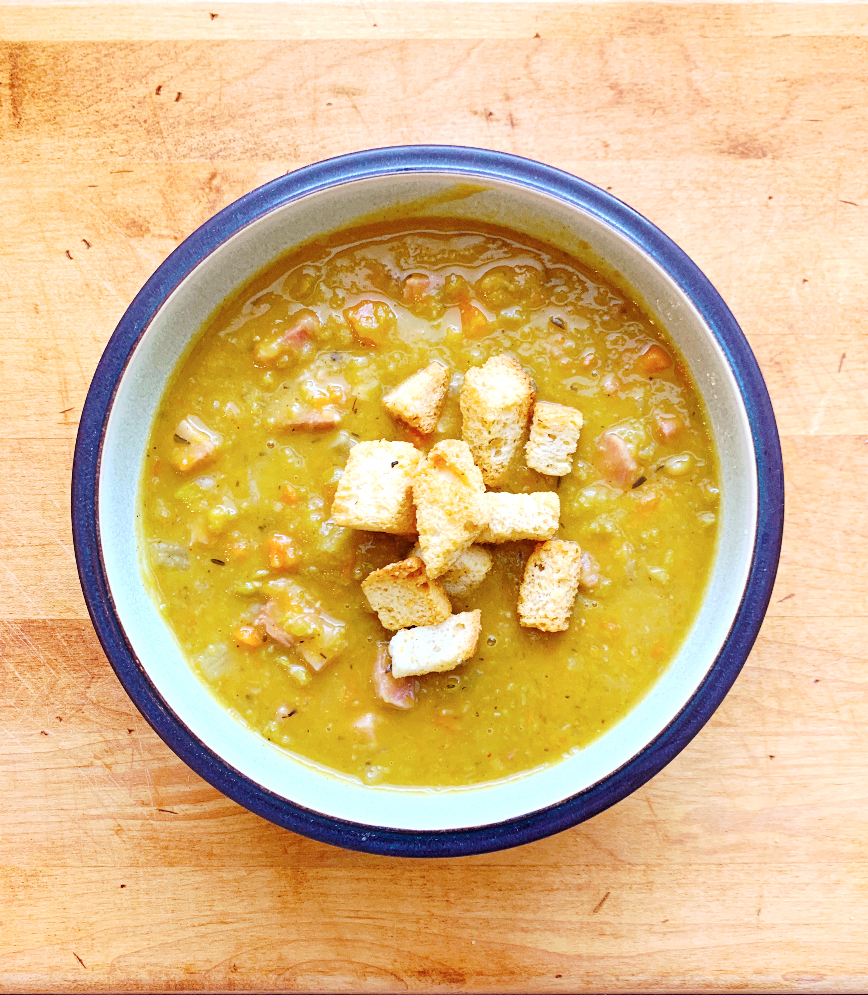 Ham and split pea soup with croutons in a bowl on a butcher block.