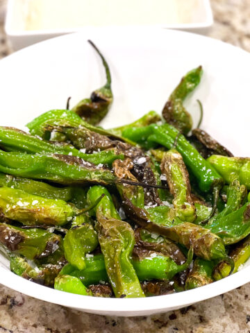 Blistered shishito peppers in a white bowl on a counter.