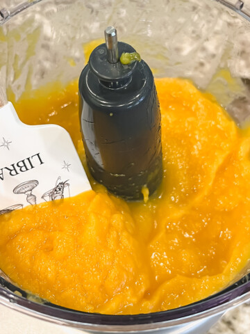Pumpkin puree with a white spatula in a food processor on a counter top.