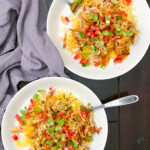 Two bowls of buffalo chicken spaghetti squash with forks on a dark tabletop with a gray napkin