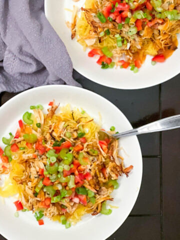 Two plates of buffalo chicken spaghetti squash on white dishes with gray napkins on a black table.