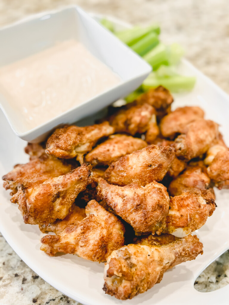 chicken wings on a white platter with celery and yogurt dip