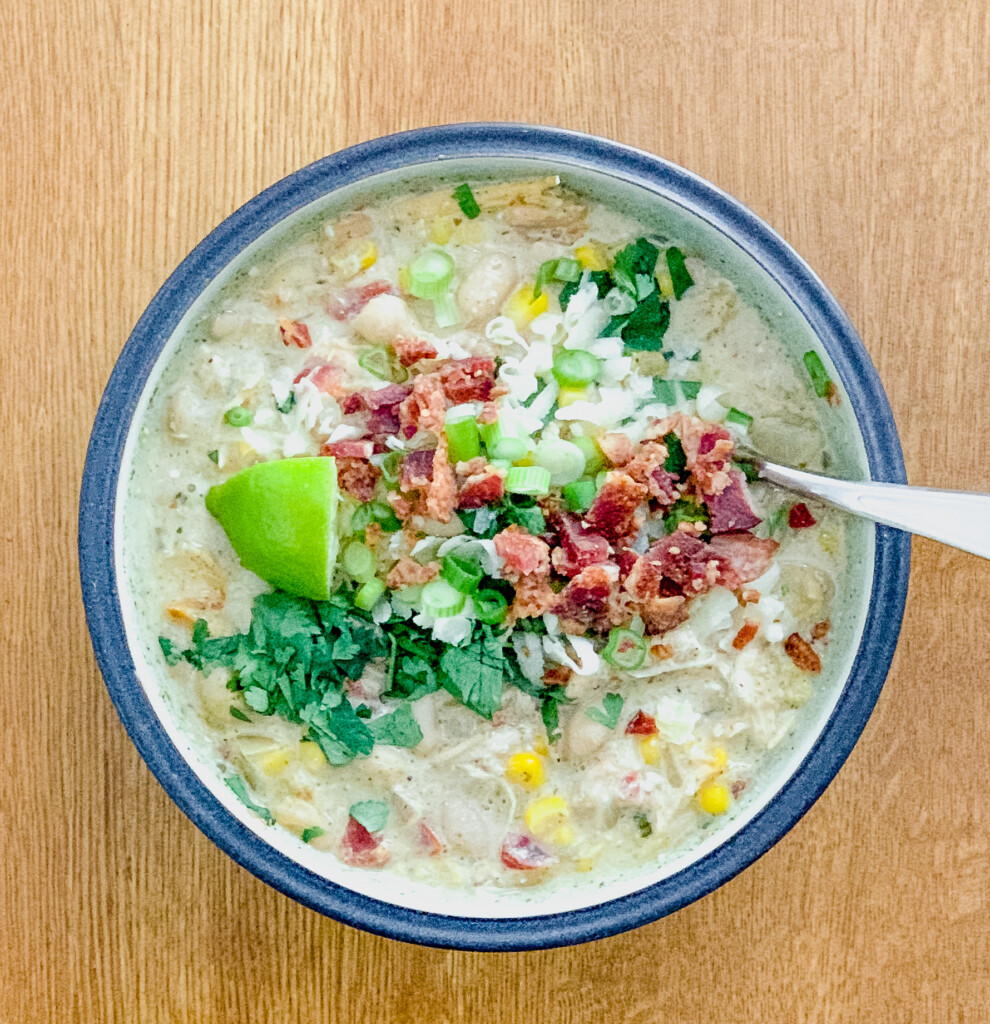 Bowl of white chicken chili with a spoon on a wood table