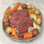 Corned beef with cabbage, potatoes and carrots on a silver platter on a white granite countertop