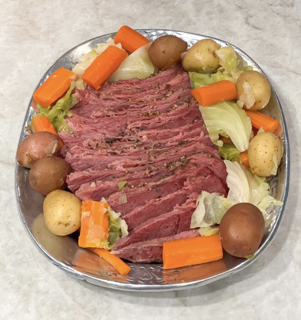Corned beef with cabbage, potatoes and carrots on a silver platter on a white granite countertop