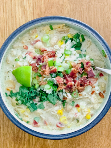 A bowl of white chicken chili on a wooden table.