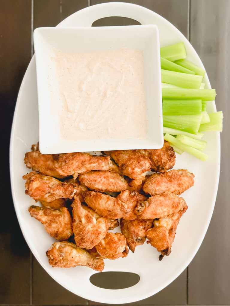 chicken wings on a white platter with celery and yogurt dip