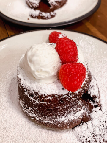 Chocolate lava cake with vanilla ice cream, raspberries and powdered sugar on a white plate