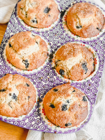 Blueberry Muffins in a muffin pan on a tea towel and wooden table
