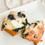 Bakery style blueberry muffin cut in half with a pat of butter on a white plate