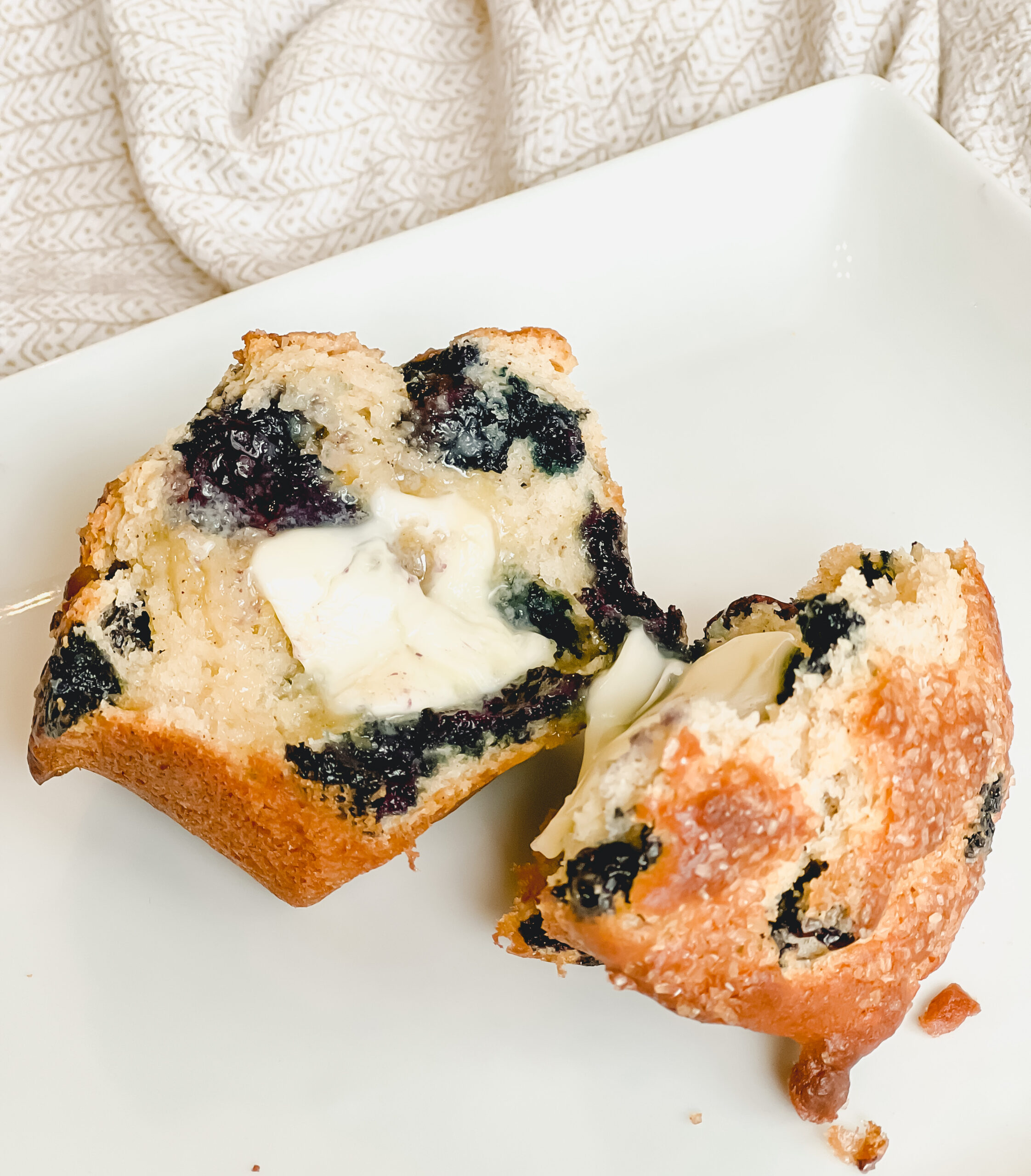 Blueberry muffin cut in half with a pat of butter on a white plate