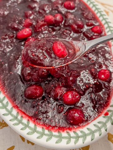 Cranberry sauce with a spoon in a dish on a gold and white tablecloth