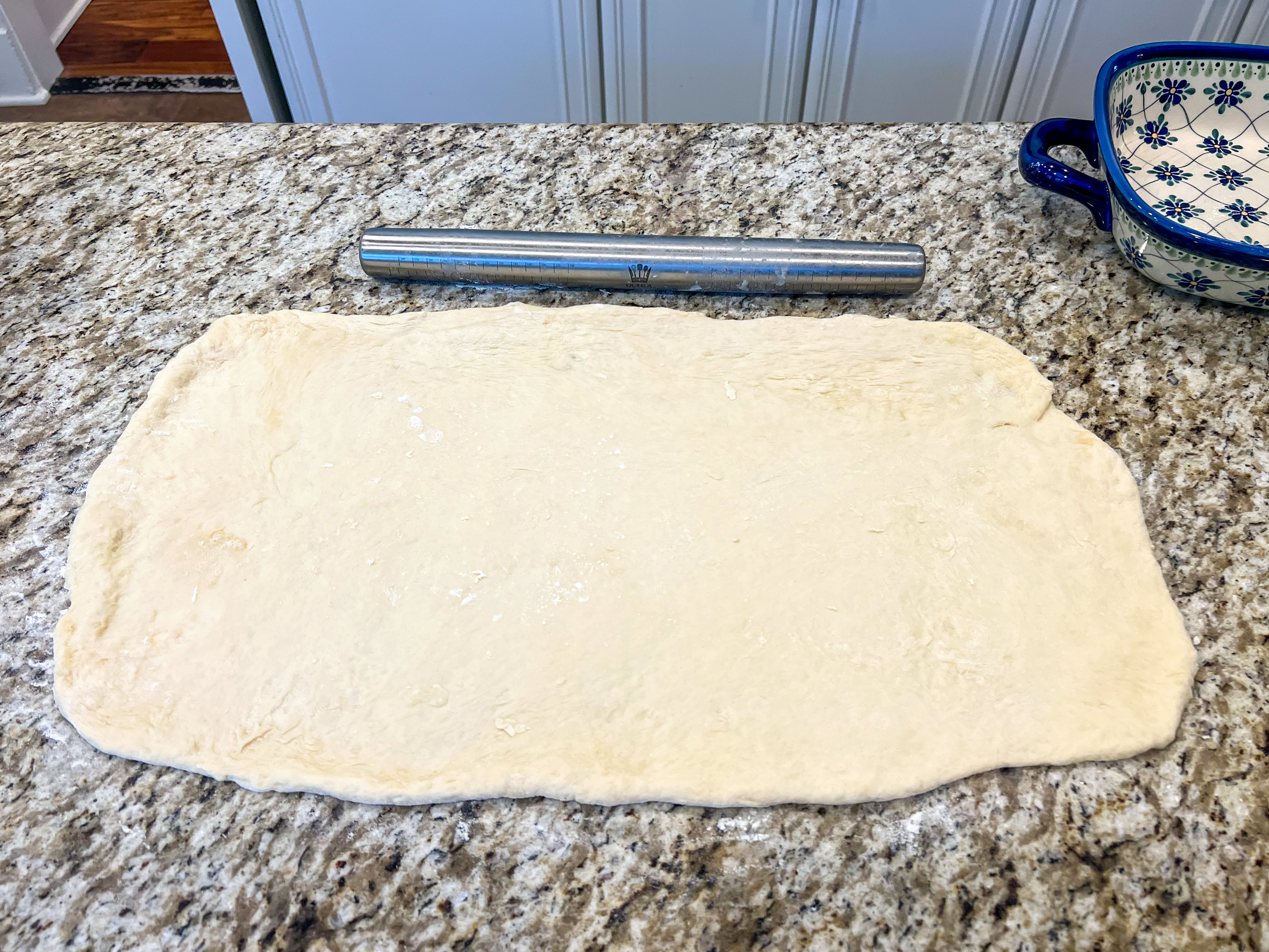 Cinnamon roll dough rolled out on a countertop with a rolling pin.
