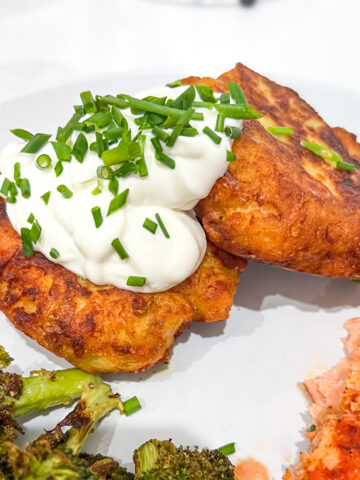 Mashed potato cakes topped with sour cream and chives on a white plate.