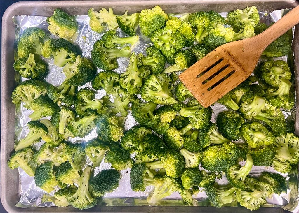 Broccoli florets on a foil-lined sheet pan with a spatula.