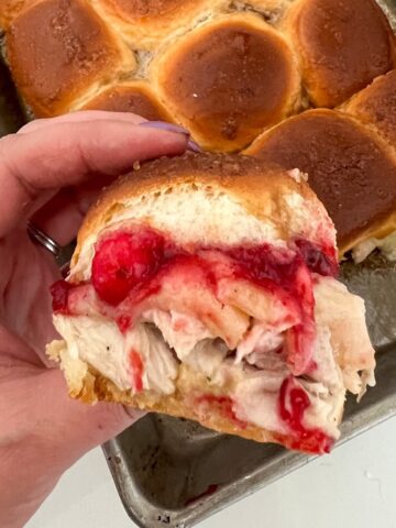 A turkey slider with cranberry sauce above a pan of turkey sliders.