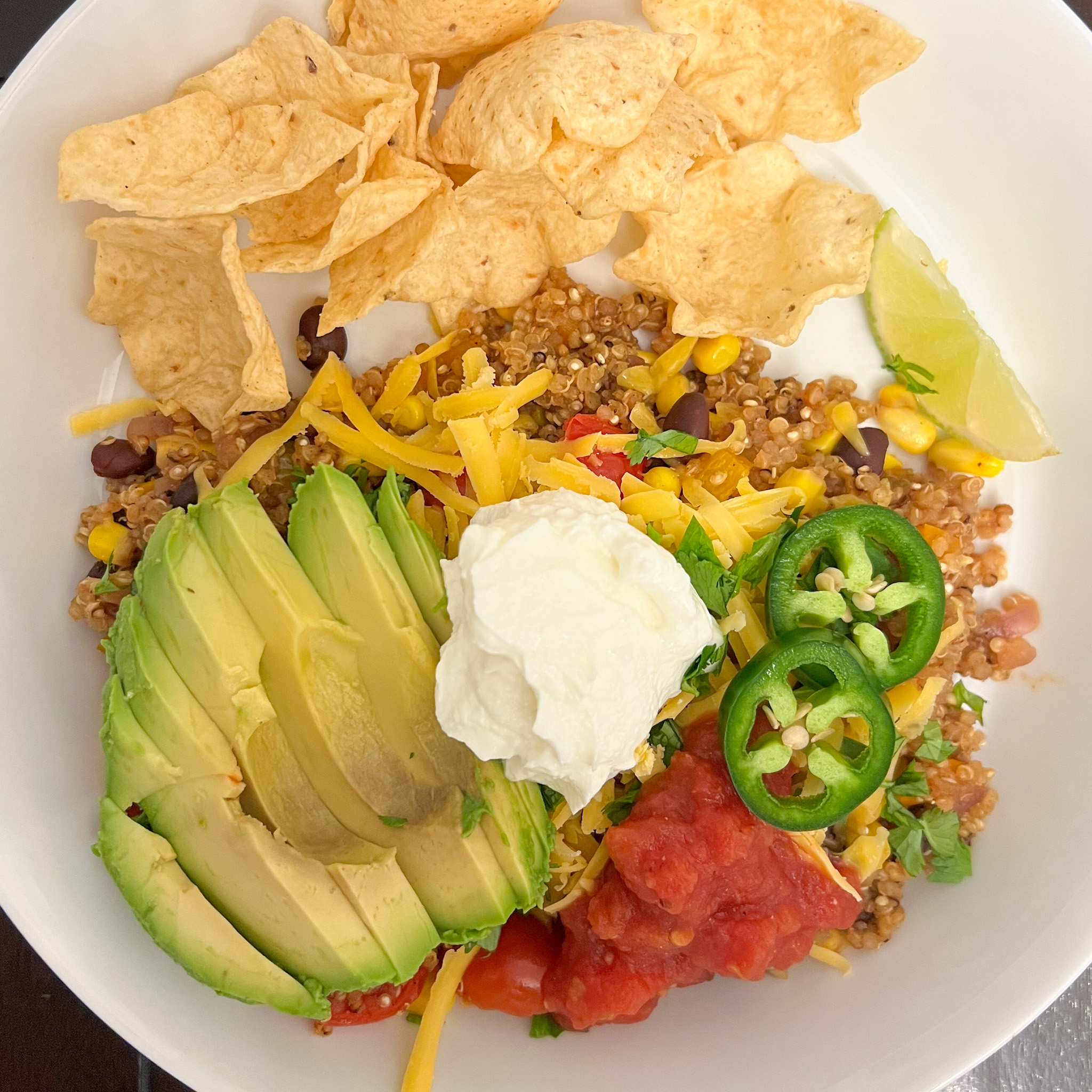 Mexican quinoa on a white plate with chips, salsa, avocado, Greek yogurt, cheese, and jalapeño slices.