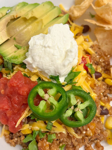 Mexican quinoa on a white plate with chips, salsa, avocado, Greek yogurt, cheese, and jalapeño slices.