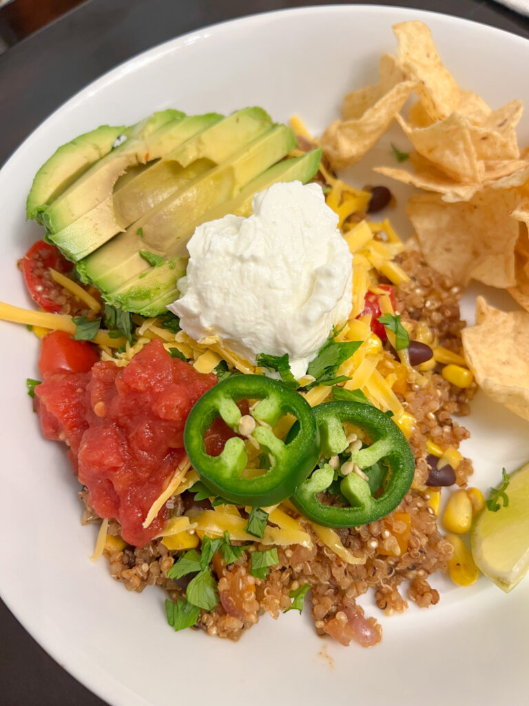 Mexican quinoa on a white plate with chips, salsa, avocado, Greek yogurt, cheese, and jalapeño slices.