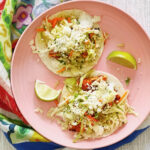 Blackened fish tacos on a pink plate with lime wedges