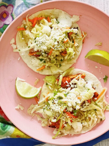 Blackened fish tacos on a pink plate with lime wedges