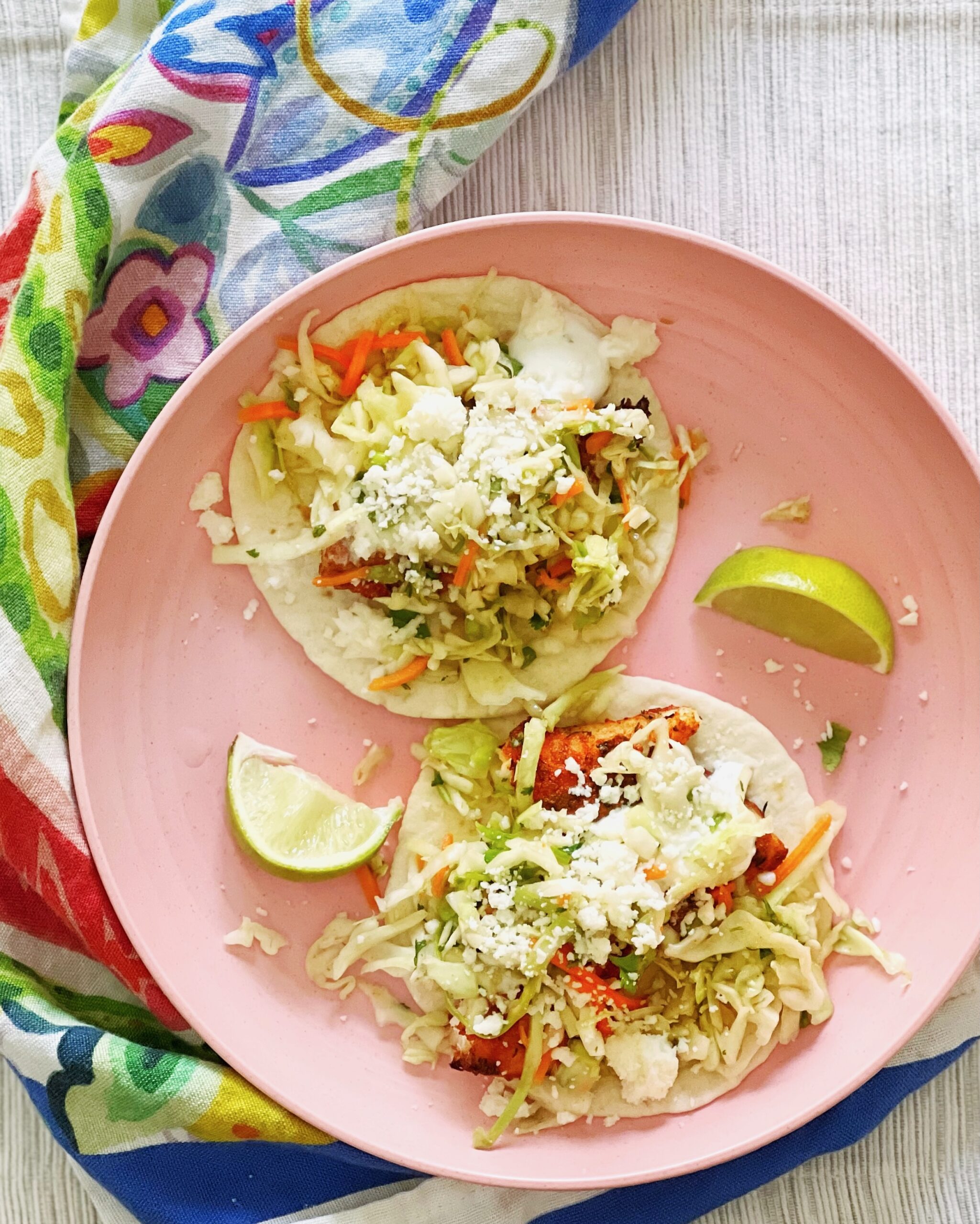 Blackened fish tacos on a pink plate with lime wedges