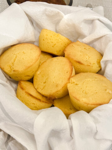 Cornbread muffins with corn in a white flour sack towel-lined basket
